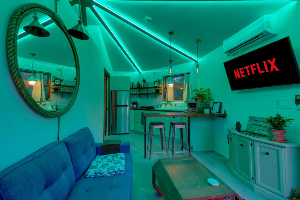 Interior of Stanley on Shellmate Island lit with teal LED ceiling lighting, showing the blue sofa, round mirror, kitchen bar and Netflix on the TV