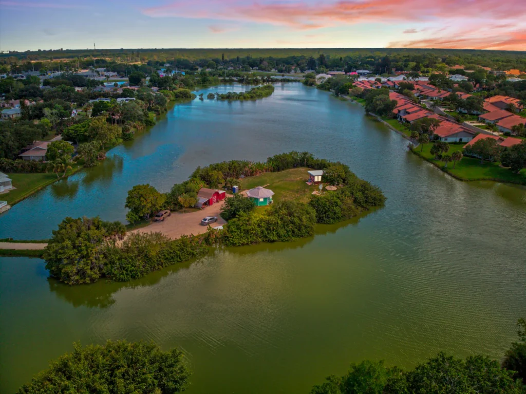 Wide aerial view of Shellmate Island surrounded by lake water in Sarasota, Florida, with tropical trees and the city in the distance at sunset