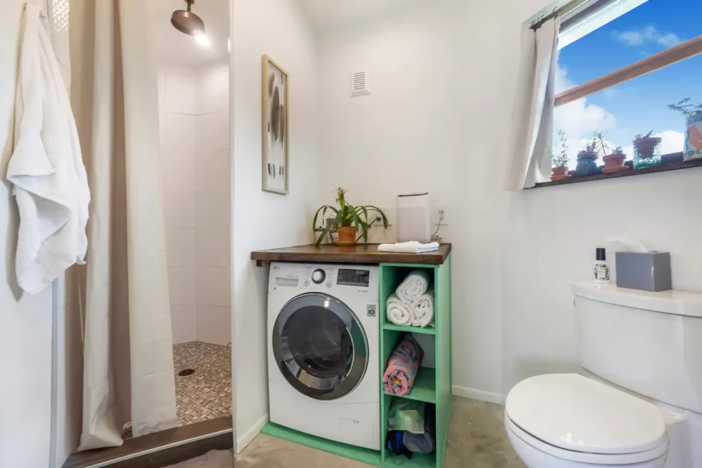 Bathroom in Stanley on Shellmate Island with a walk-in shower behind a curtain, a front-loading washer and dryer under a wood counter, white walls and a towel hook