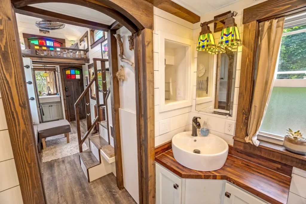Bathroom sink area in Tiffany The Tiny Home with a vessel sink on a wood countertop, stained glass lamp, and a view through to the staircase and living area