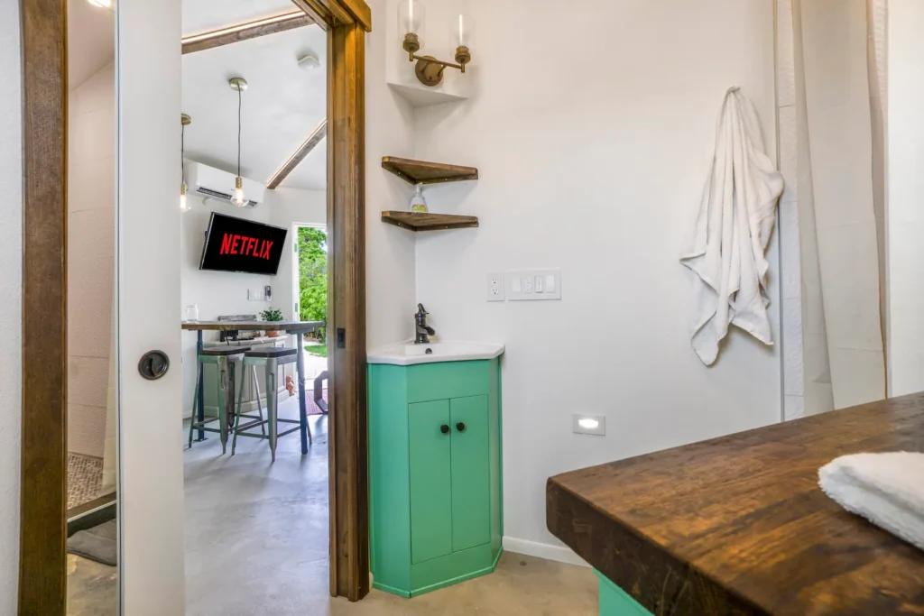 View from the bathroom doorway in Stanley on Shellmate Island toward the kitchen bar and TV, with a mint-green cabinet and wood shelving