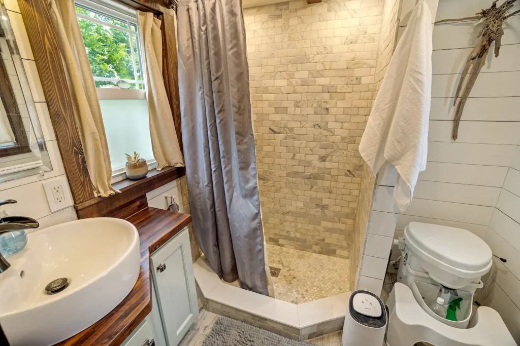 Bathroom in Tiffany The Tiny Home with a tiled walk-in shower, vessel sink, white shiplap walls, and a composting toilet