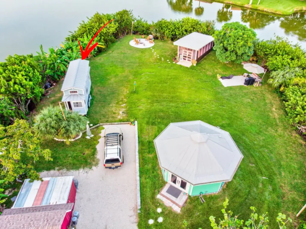 Aerial view of Shellmate Island in Sarasota, Florida, showing Tiffany The Tiny Home on wheels (marked with a red arrow) and Stanley the mint-green octagonal tiny house, with the lawn, driveway and fire pit