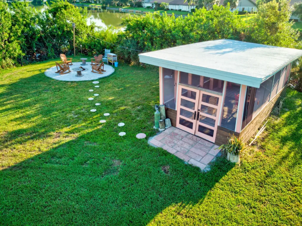 Aerial view of the Shellmate Island fire pit with Adirondack chairs and stepping-stone path next to the screened lounge roof, surrounded by lawn and trees