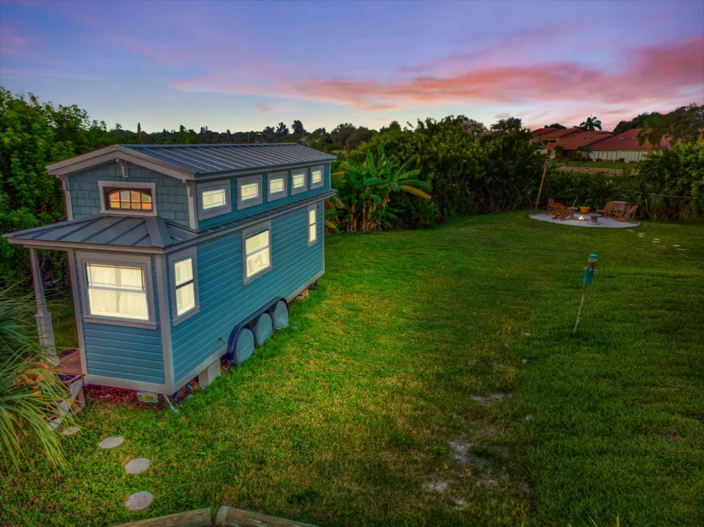 Exterior of Tiffany The Tiny Home, a blue tiny house on wheels with a metal roof, parked on the lawn of Shellmate Island in Sarasota, Florida, at sunset