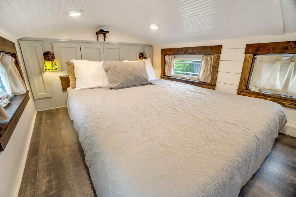 Downstairs bedroom in Tiffany The Tiny Home with a memory foam bed, white shiplap walls, wood-trimmed windows, and sconce lighting