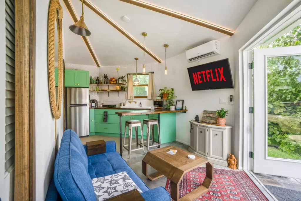 Living room in Stanley on Shellmate Island with a blue sofa, round rope mirror, mini-split air conditioner, and the mint-green kitchen and bar seating beyond