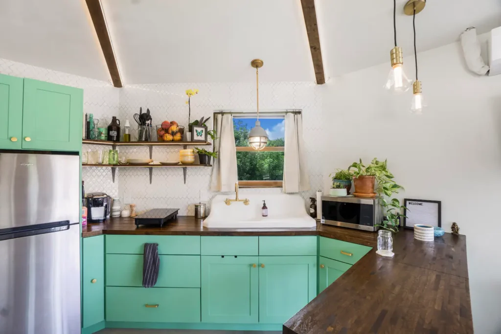 Kitchen in Stanley on Shellmate Island with mint-green cabinets, a stainless refrigerator, farmhouse sink under a window, open shelving and pendant lights