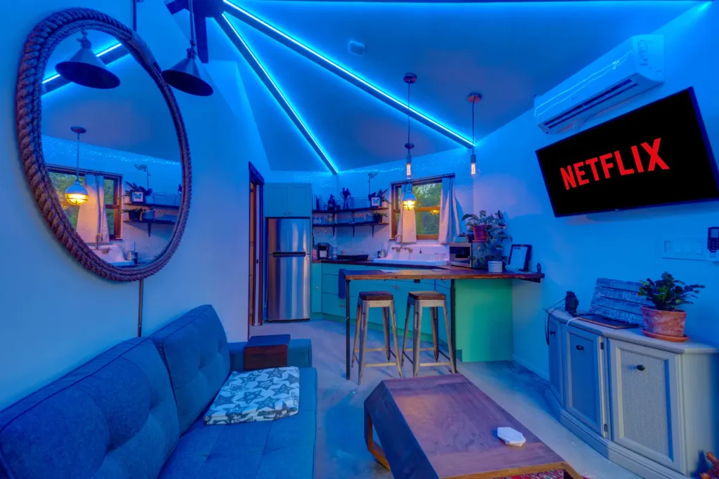 Interior of Stanley on Shellmate Island lit with blue LED strip lighting along the octagonal ceiling beams, showing the blue sofa, round mirror, kitchen bar and Netflix on the TV