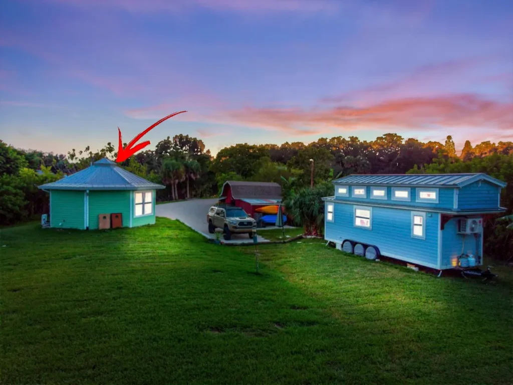 Aerial view at sunset of Stanley, the mint-green octagonal tiny house on Shellmate Island in Sarasota, Florida, marked with a red arrow, with Tiffany The Tiny Home and the red shed nearby
