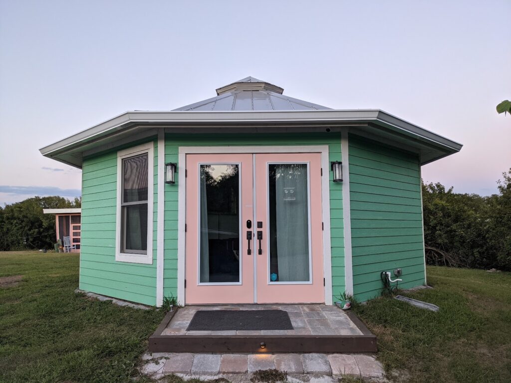 Shellmate Island, a mint-green octagonal 320 sq ft tiny home with white French doors and a pink door frame on a private island in Sarasota, Florida