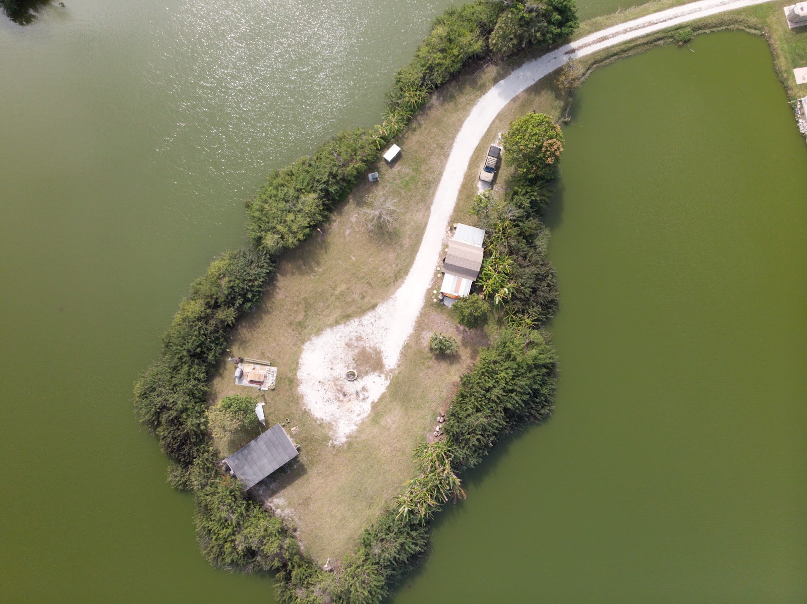 Drone photo of a small private island in a Sarasota lake with a winding shell path, two tiny homes, and a causeway to the mainland