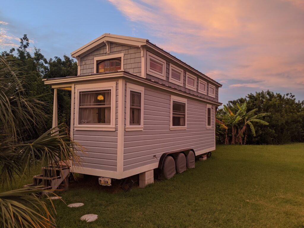 Tiffany The Tiny Home, a 270 sq ft tiny house on wheels with a loft and white trim, glowing in sunset light on a private island in Sarasota